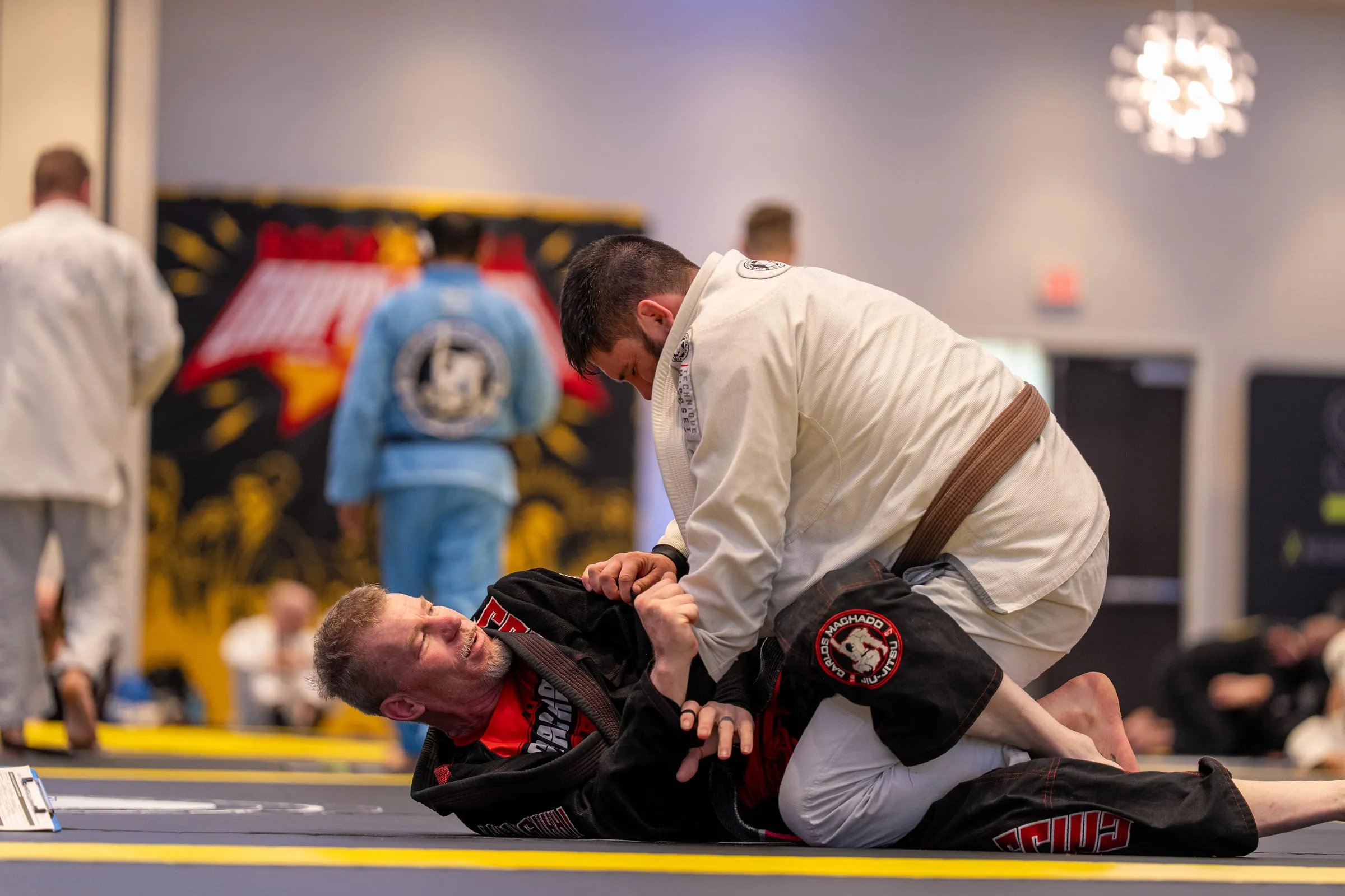 Two adults drilling a guard pass on a crowded mat