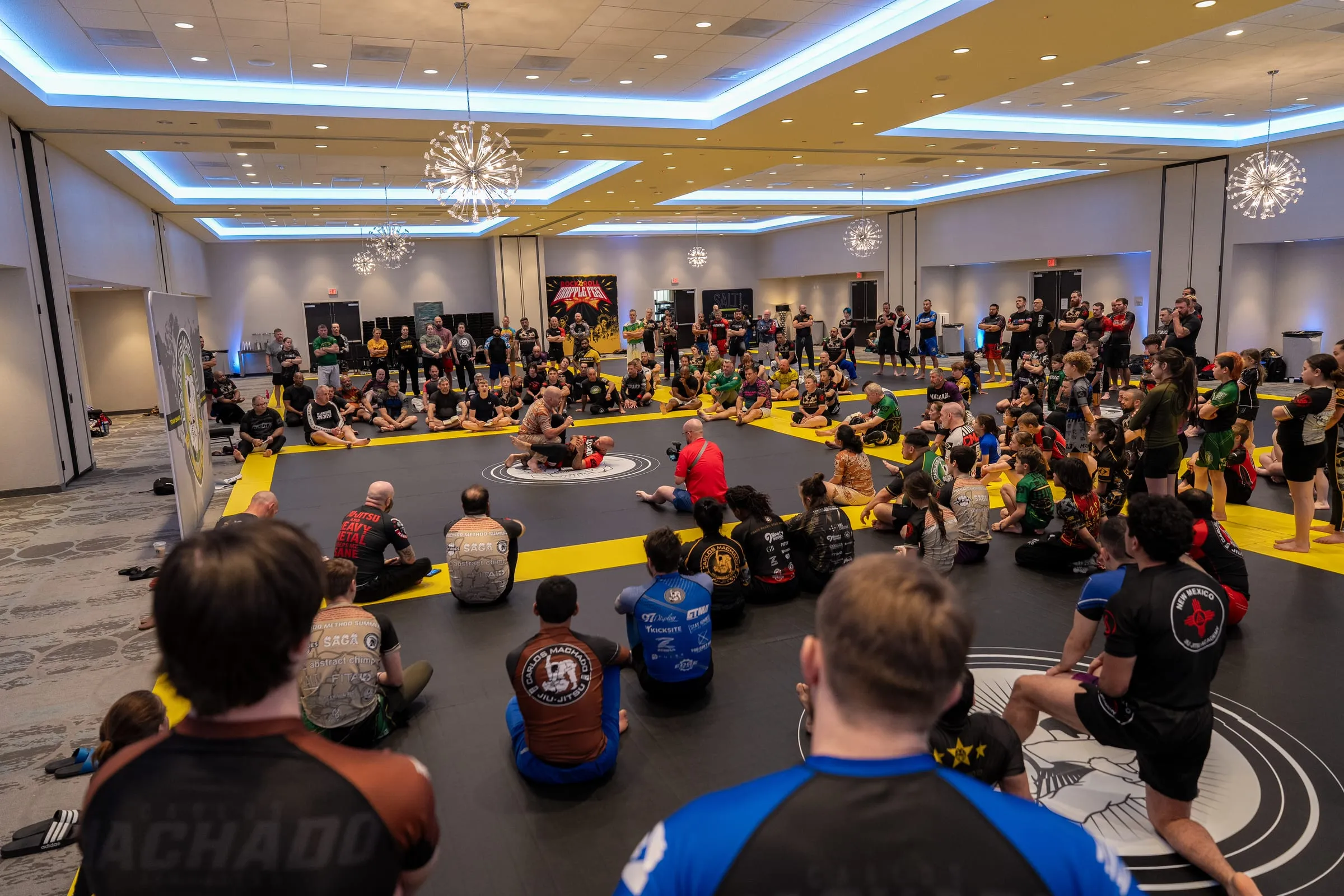 Attendees seated in a ring around the mat during a Machado Method seminar
