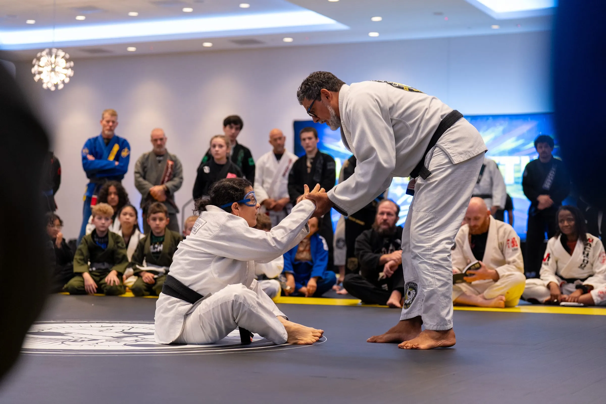 A senior instructor demonstrating a technique on a seated black-belt partner